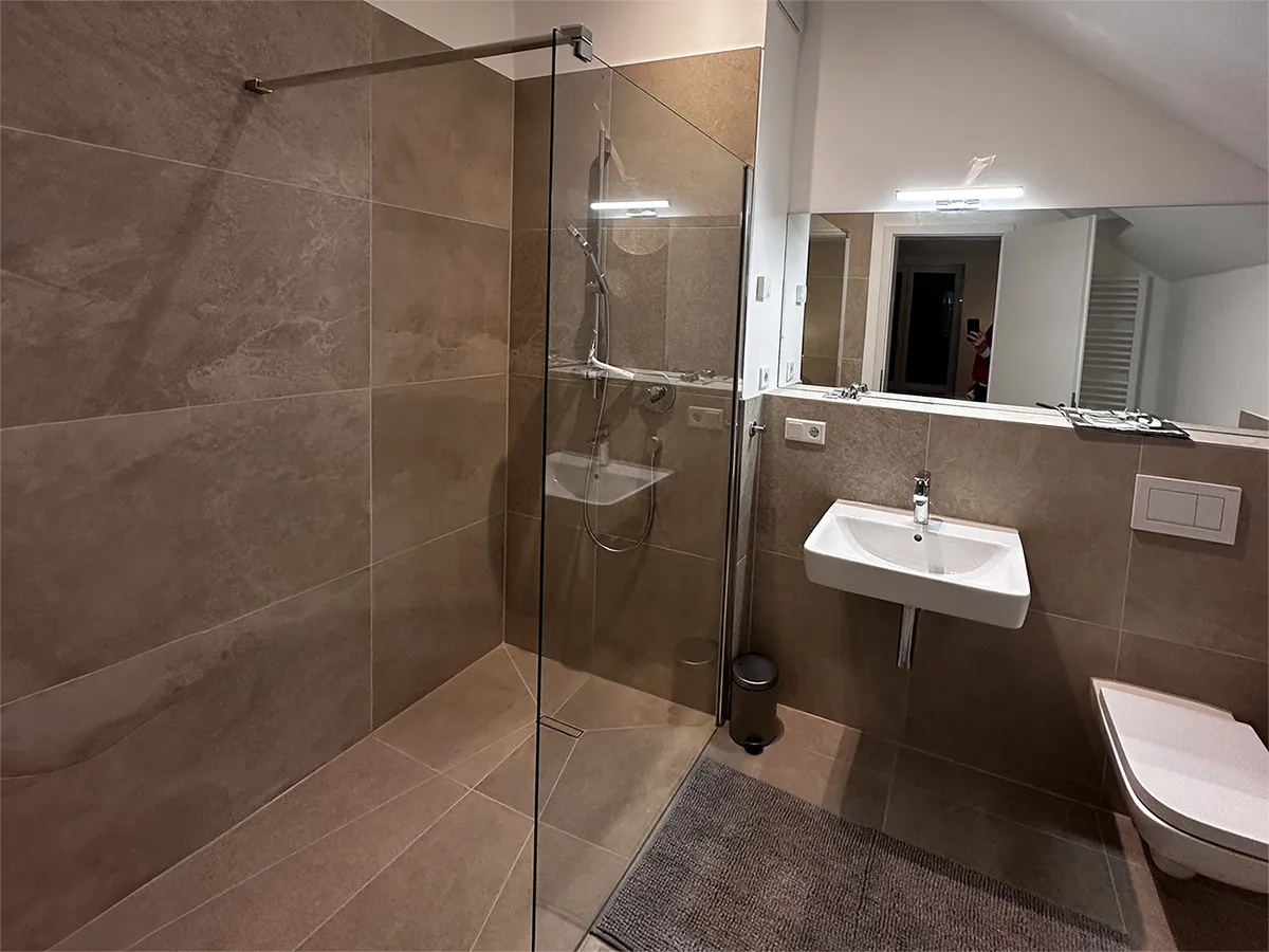 Modern eingerichtetes Bad mit Fußbodenheizung, Handtuchtrockner und bodengleicher Dusche.